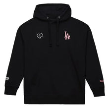 A black pullover hoodie with a white heart outline logo on the left chest and a pink 'LA' logo on the right chest, displayed on a light gray background.