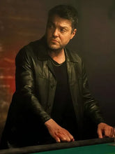 Man in a leather jacket sitting at a pool table with a dark background