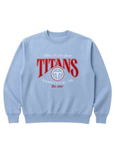 A light blue crewneck sweatshirt featuring a red and white graphic print on the front that reads 'TITANS NASHVILLE, TN' with a circular logo, displayed on a neutral light gray background.
