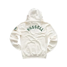 An off-white hooded sweatshirt shown from the back, featuring 'RUSSELL' printed in dark green arched block letters across the upper back and a small circular patch on the left sleeve, set against a solid light gray background.