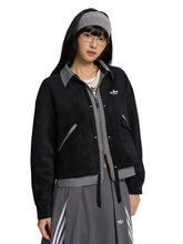 A model wearing a black Adidas zip-up jacket with gray trim, a gray headband, and a gray skirt with white stripes, set against a solid light gray background.