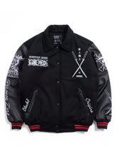 A black varsity-style bomber jacket with black leather sleeves, featuring white graphic prints and text on the front and sleeves, red and black striped ribbed cuffs and hem, and snap-button closure.